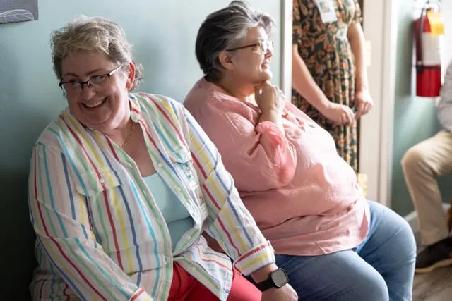 Two people sitting together on a couch in the practice, mid-conversation and laughing.
