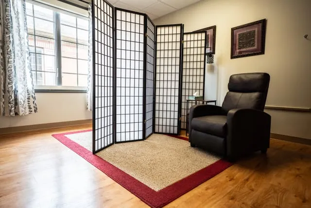 A therapy room with a recliner, a folding screen and a patterned rug.